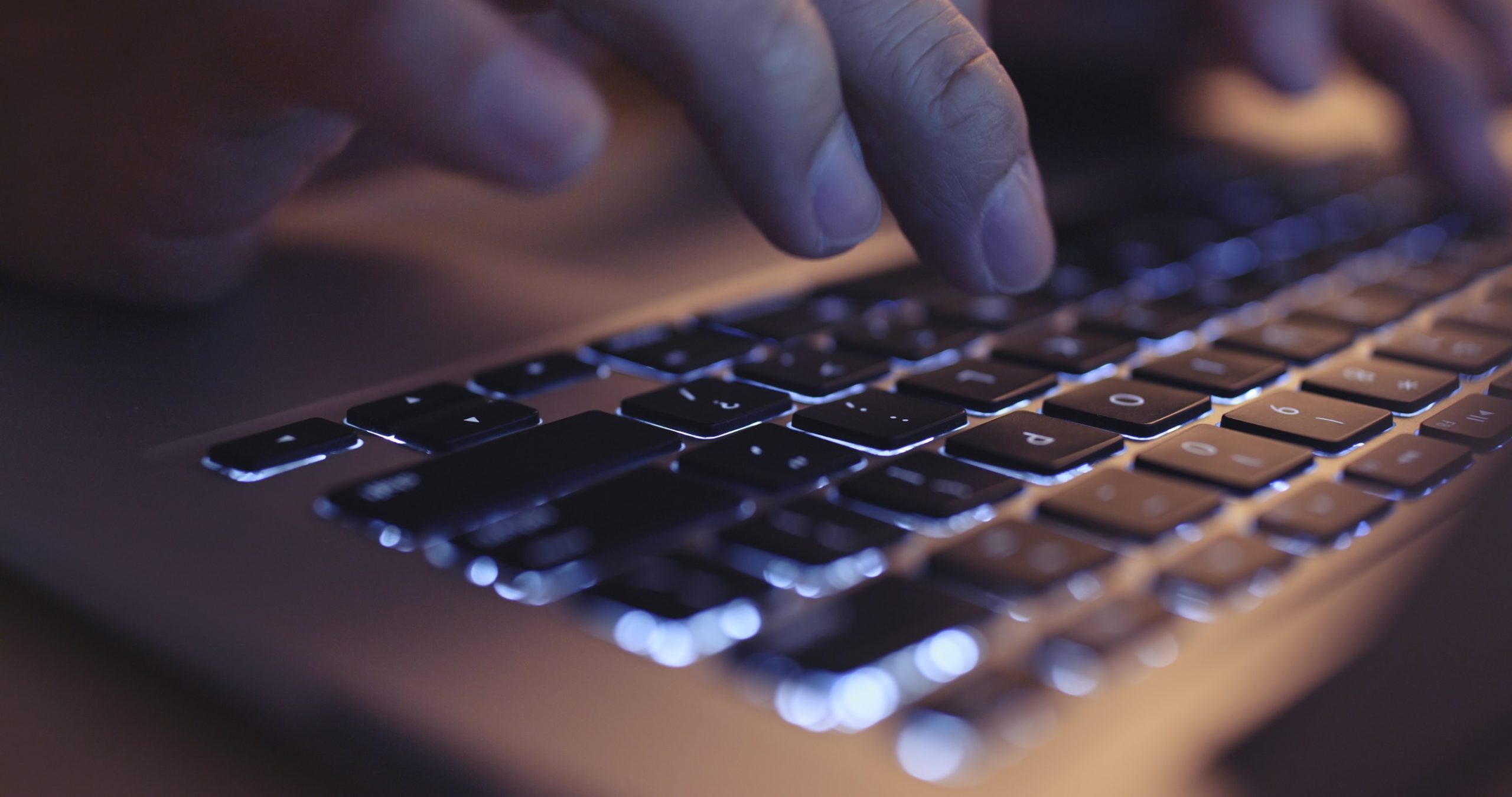 Close-up of a man's hands typing on a laptop keyboard